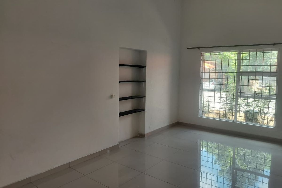 An empty living room featuring polished tiled flooring, a large window with security bars, and built-in wall shelving.