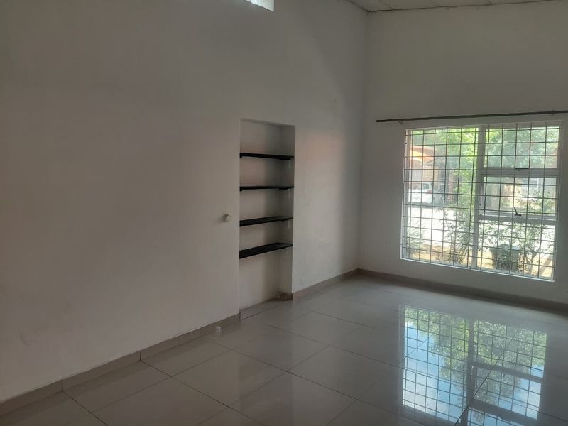 An empty living room featuring polished tiled flooring, a large window with security bars, and built-in wall shelving.