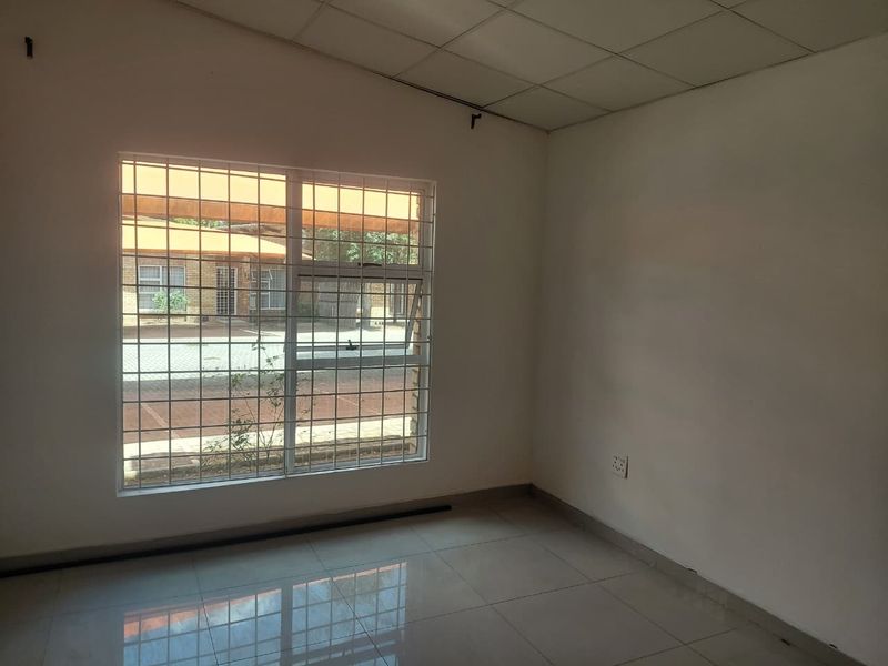 An empty bedroom featuring tiled flooring, a drop ceiling, and a window fitted with security bars, offering a blank canvas for renovation.