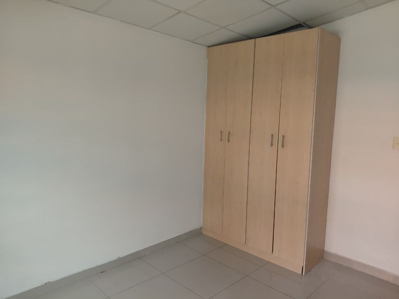 A clean, empty bedroom featuring neutral tiled flooring, a drop ceiling, and a functional built-in wooden wardrobe.