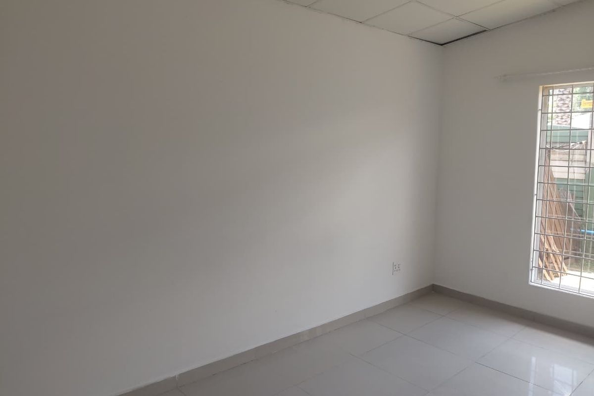 A bright, empty bedroom featuring tiled flooring, a drop ceiling, and a window fitted with security bars.