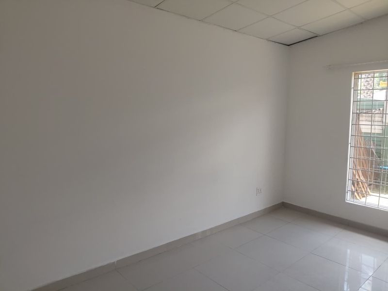 A bright, empty bedroom featuring tiled flooring, a drop ceiling, and a window fitted with security bars.