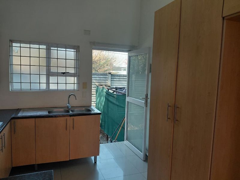 A functional kitchen area featuring laminate cabinetry, a double sink, tiled flooring, and direct access to the rear exterior through a security door.