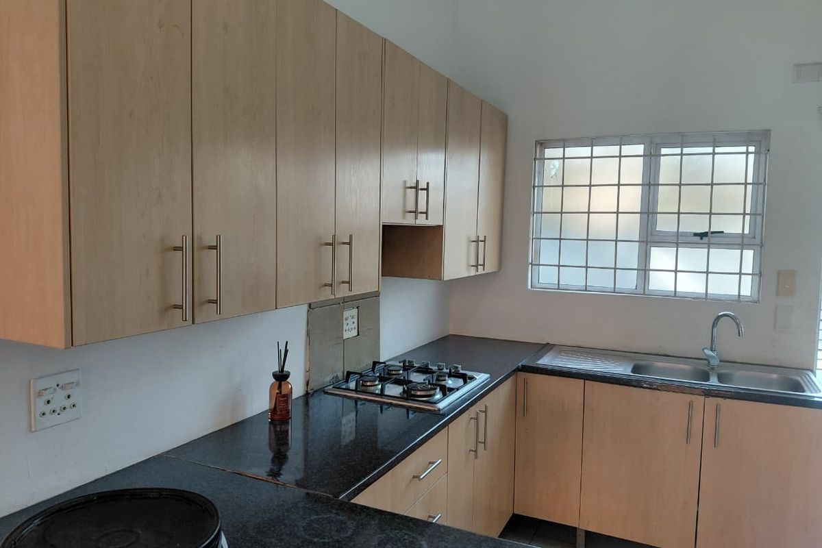 Functional kitchen featuring light wood cabinetry, granite countertops, a gas hob, and a stainless steel sink with security-barred window.