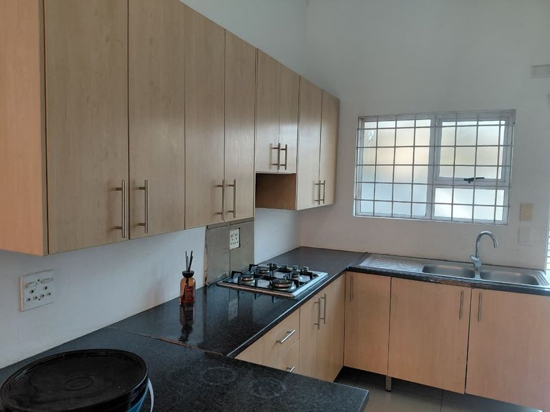 Functional kitchen featuring light wood cabinetry, granite countertops, a gas hob, and a stainless steel sink with security-barred window.