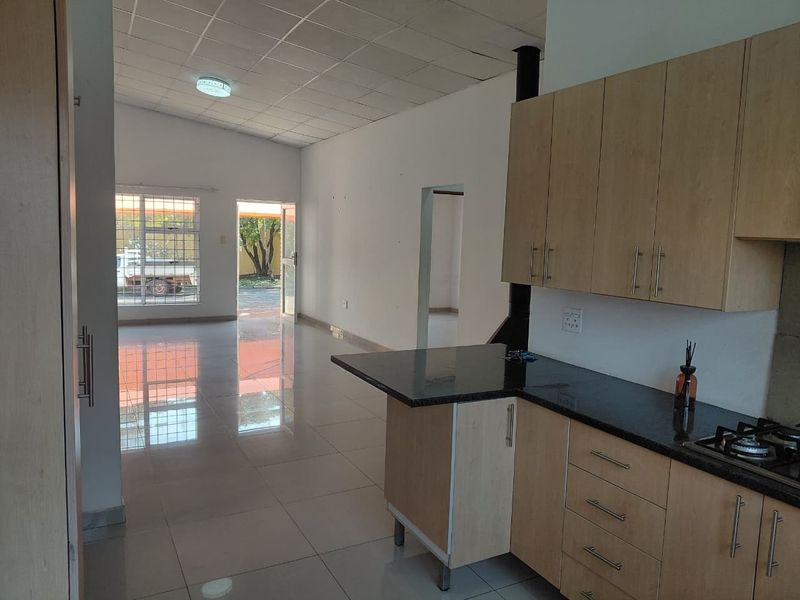 Open-plan kitchen and living area featuring light wood cabinetry, granite countertops, gas hob, tiled flooring, and direct access to the exterior.
