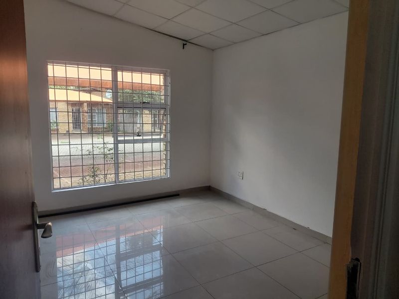 An empty bedroom featuring tiled flooring, security bars on the window, and a drop ceiling, offering a blank canvas for renovation.