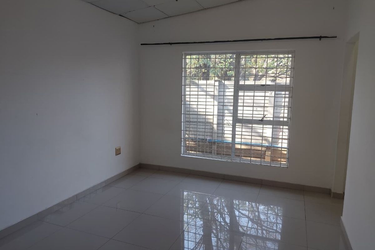An empty bedroom featuring tiled flooring, a window with security bars, and a drop ceiling, offering a blank canvas for personalization.
