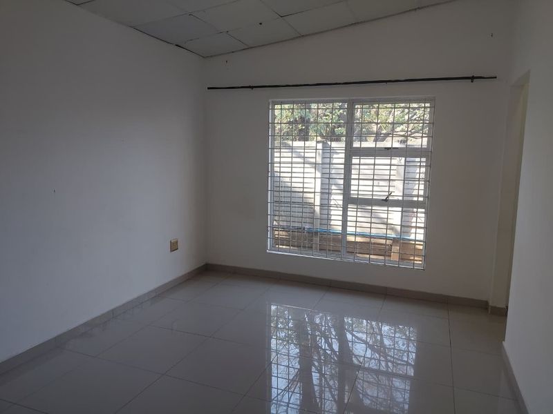 An empty bedroom featuring tiled flooring, a window with security bars, and a drop ceiling, offering a blank canvas for personalization.
