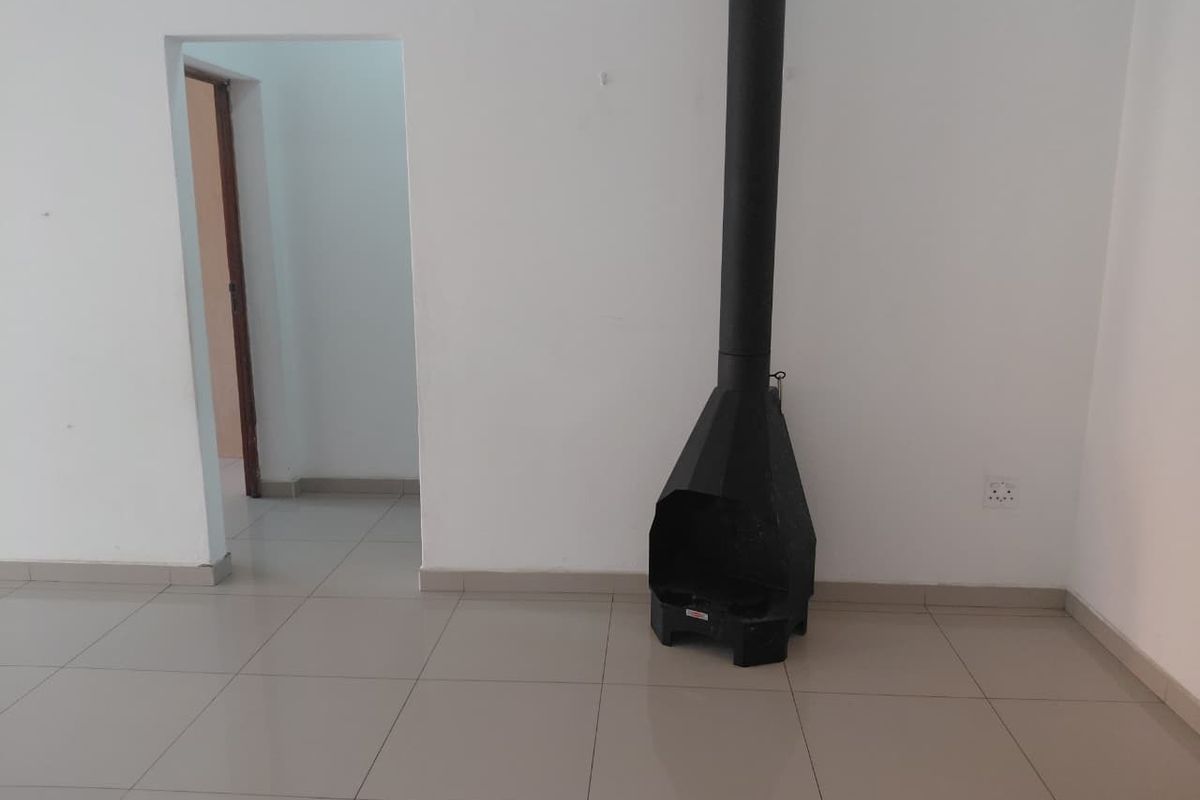 An empty living room featuring tiled flooring and a black freestanding fireplace, providing a blank canvas for interior design.