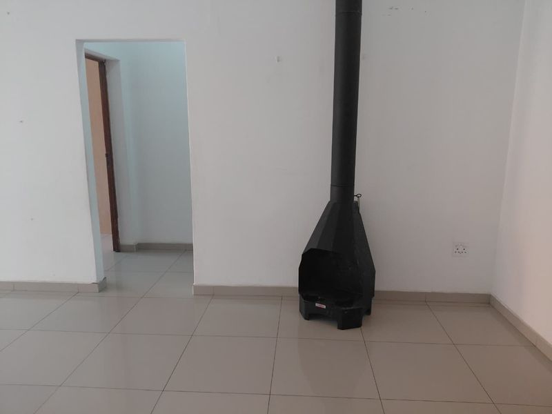 An empty living room featuring tiled flooring and a black freestanding fireplace, providing a blank canvas for interior design.