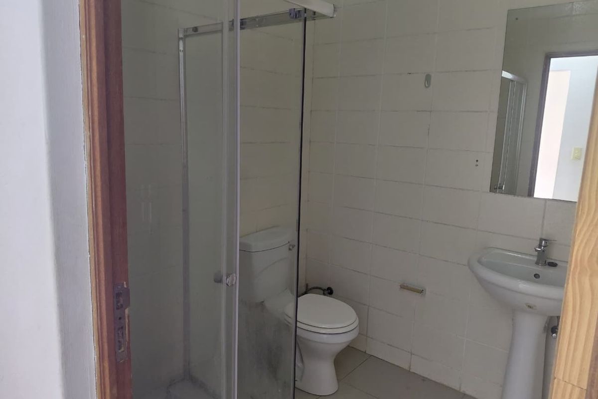 A functional bathroom featuring a shower enclosure, pedestal basin, and toilet, finished with white wall tiles and floor tiling.