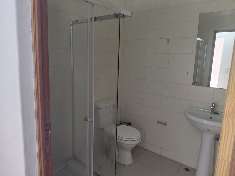 A functional bathroom featuring a shower enclosure, pedestal basin, and toilet, finished with white wall tiles and floor tiling.