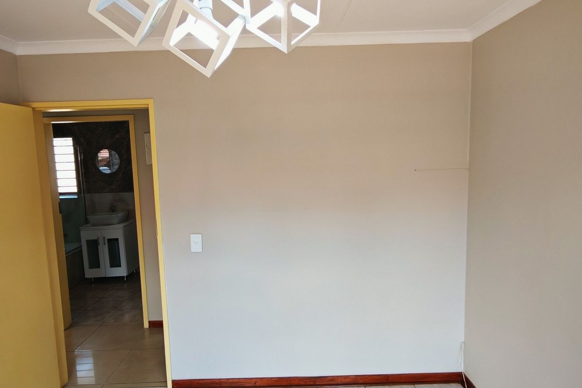 An empty bedroom featuring neutral wall tones, timber skirting boards, and a view into the adjacent bathroom.
