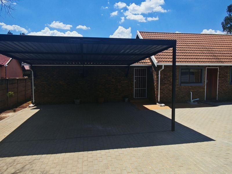 Front exterior view featuring a modern metal carport, paved driveway, and brick house facade with a tiled roof.