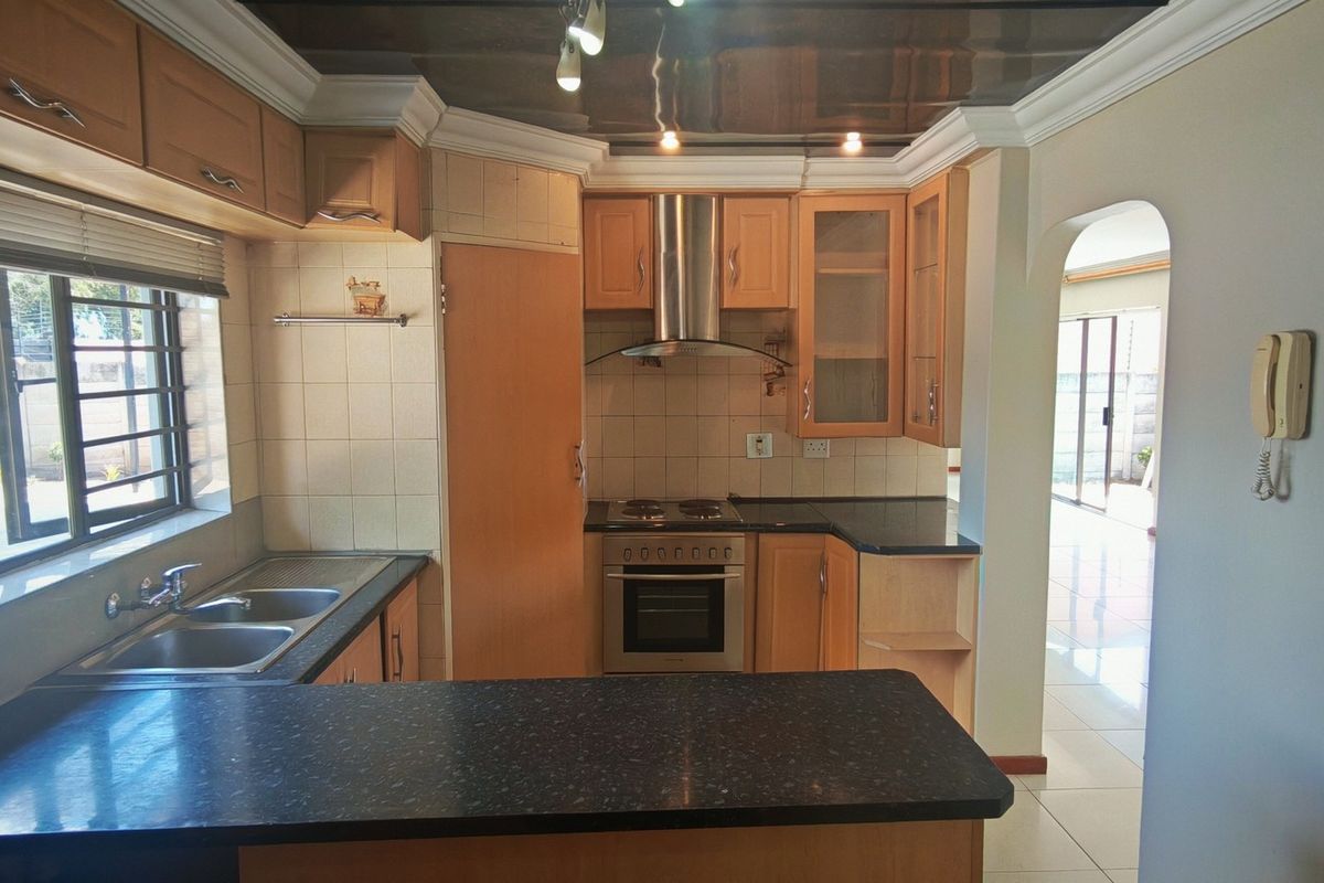 A functional kitchen featuring wooden cabinetry, laminate countertops, a built-in oven with extractor fan, and tiled finishes throughout.