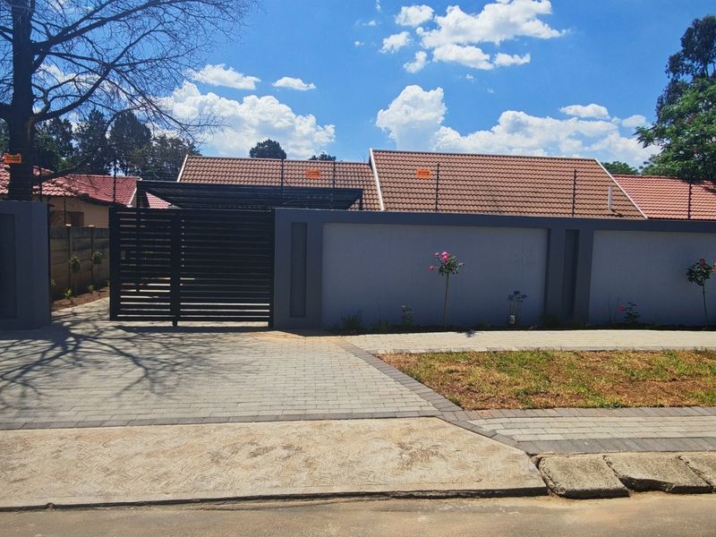 Front view of the property featuring a secure perimeter wall, sliding gate, paved driveway, and a well-maintained tiled roof structure.