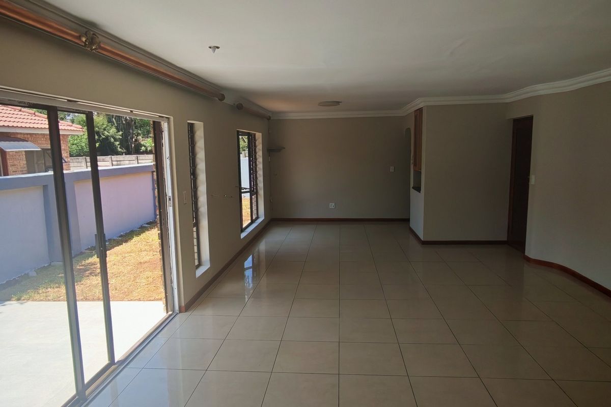 Spacious, empty living area featuring neutral tiled flooring, cove cornicing, and large sliding glass doors providing direct access to the outdoor patio area.