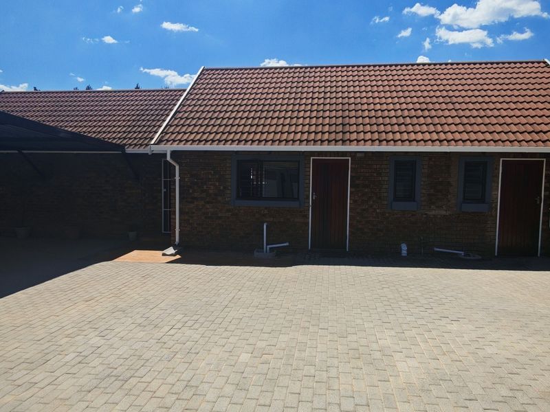 A well-maintained brick house exterior featuring a tiled roof, paved driveway, and a covered carport area.