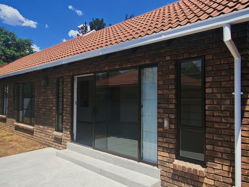 Rear view of the house featuring a face brick facade, tiled roof, concrete patio, and sliding glass doors leading into the interior.
