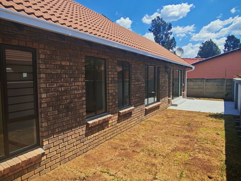 Rear view of the house featuring a face brick exterior, tiled roof, and a private garden area with a concrete boundary wall.