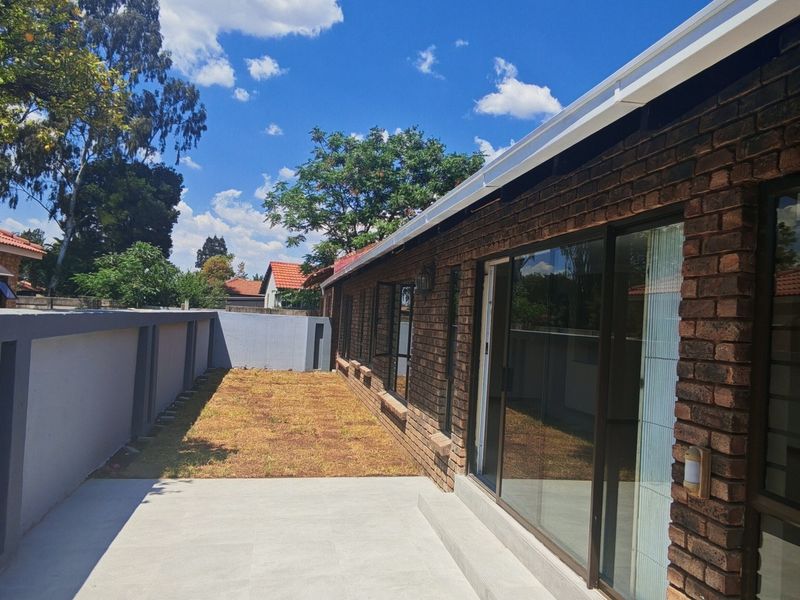 A well-maintained rear exterior featuring a face brick facade, sliding glass doors, a paved patio area, and a secure perimeter boundary wall.