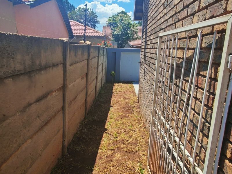 A narrow side passage featuring a facebrick exterior wall, a precast concrete boundary wall, and a metal security gate.