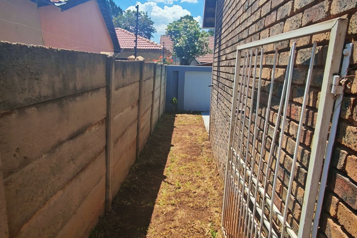 A narrow side passage featuring a facebrick exterior wall, a precast concrete boundary wall, and a metal security gate.