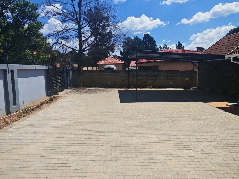 A well-maintained paved driveway featuring a covered carport, secure perimeter walling with electric fencing, and clear access to the property entrance.