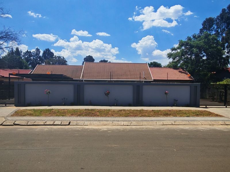 Front view of the property featuring a secure perimeter wall, tiled roof, and paved driveway access from the street.