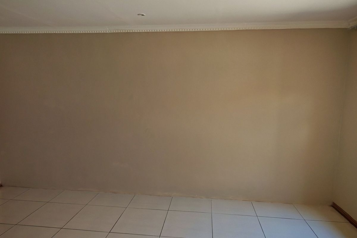 A bright, empty living room featuring neutral-toned walls, tiled flooring, and crown molding, offering a clean and versatile space ready for personalization.