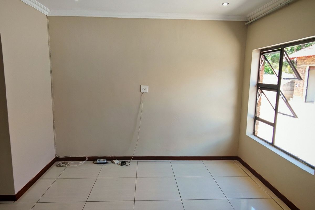 A bright, empty bedroom featuring neutral wall paint, tiled flooring, and a large aluminium-framed window allowing for natural light.