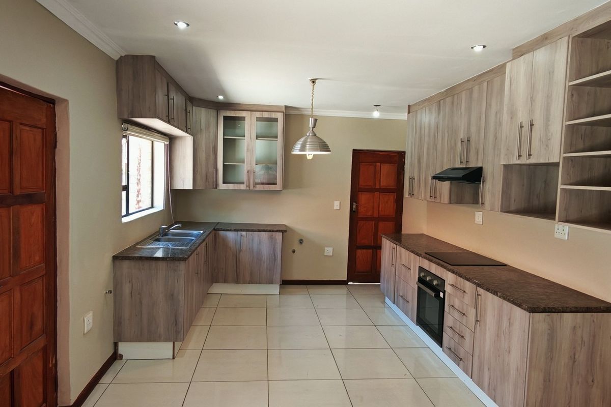 Modern kitchen featuring light wood-grain cabinetry, dark laminate countertops, built-in oven, hob, extractor fan, and tiled flooring in a clean, open layout.