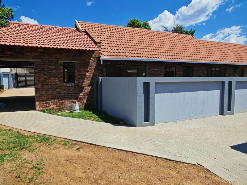 Front view of a face brick house featuring a tiled roof, paved driveway, and a modern grey boundary wall.