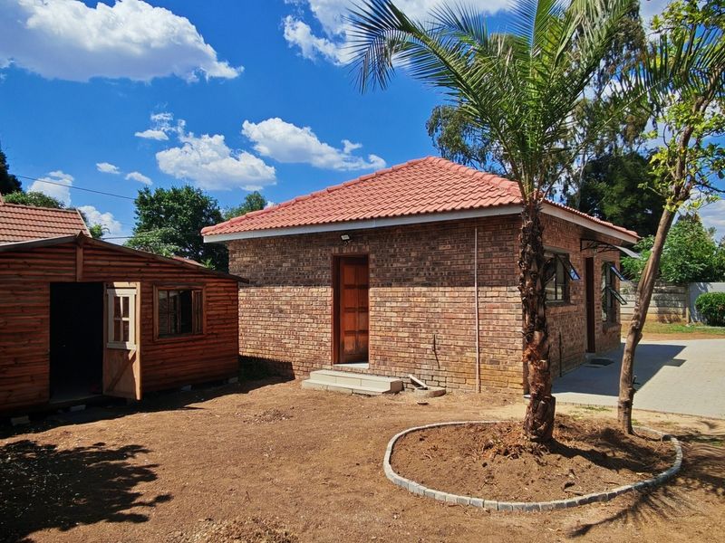 Rear view of the property featuring a face brick main structure, a wooden outbuilding, and a concrete driveway with an unlandscaped garden area.