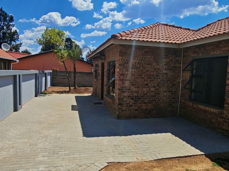 A well-maintained rear exterior view featuring a face brick facade, tiled roof, and a clean paved patio area enclosed by a boundary wall.