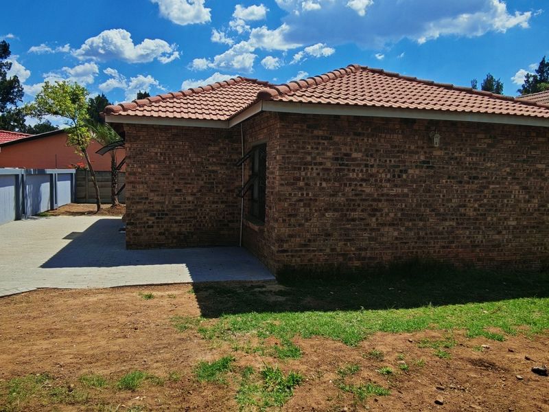Rear view of the property featuring a face brick exterior, tiled roof, and a paved patio area with surrounding boundary walls.