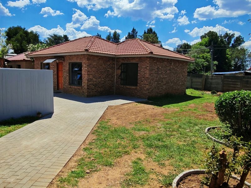 A rear view of a face brick house featuring a tiled roof, paved walkway, and a private garden area with boundary walling.