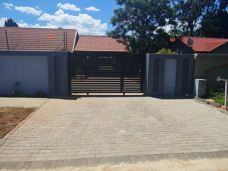 Front view of the property featuring a paved driveway, secure perimeter wall, and a modern sliding gate with electric fencing.