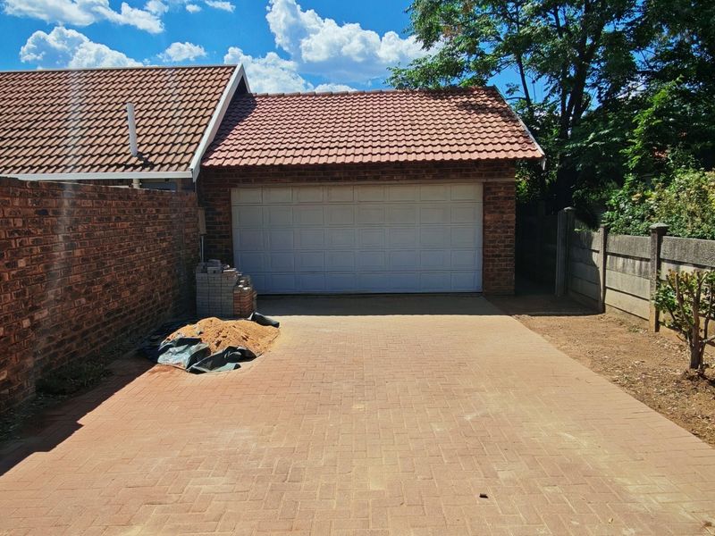 A detached garage with a tiled roof and paved driveway, featuring brick and precast concrete boundary walls.