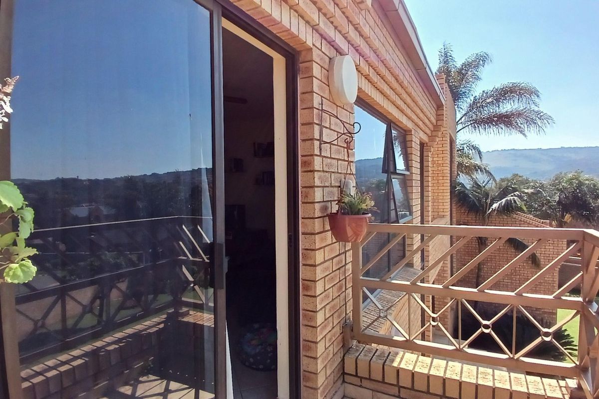 A brick-faced balcony featuring a metal balustrade and a sliding glass door providing access to the interior living space.