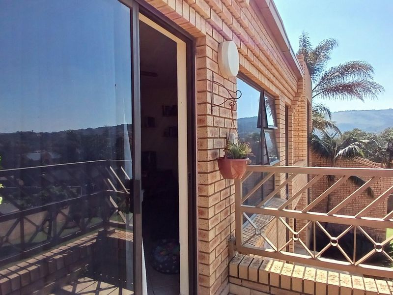 A brick-faced balcony featuring a metal balustrade and a sliding glass door providing access to the interior living space.