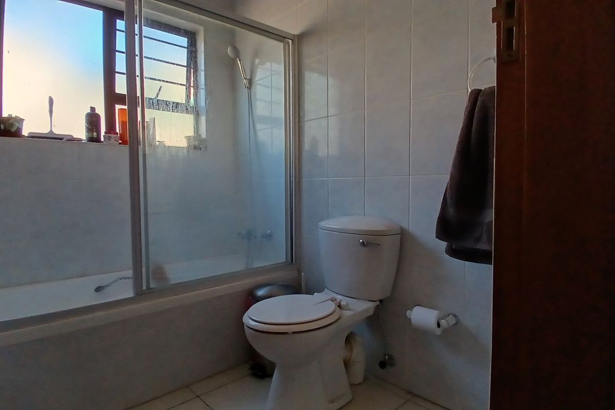 A functional bathroom featuring a bathtub with a shower screen, a standard toilet, and tiled wall and floor finishes.