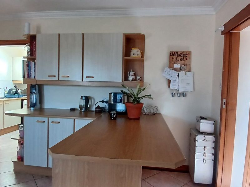 A functional kitchen area featuring built-in cabinetry, a breakfast bar, and tiled flooring, with a view into an adjacent scullery or utility space.