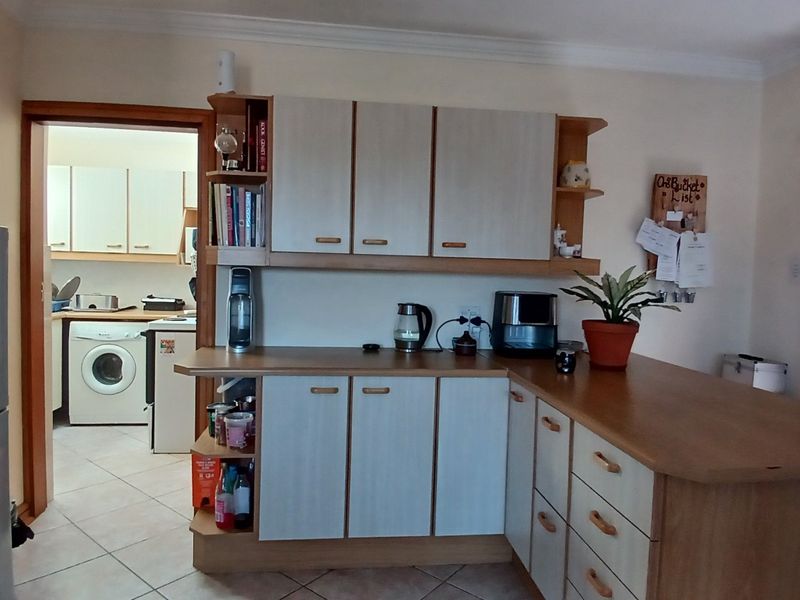 A functional kitchen featuring laminate cabinetry, ample counter space, and tiled flooring, with an adjacent laundry area visible through the doorway.