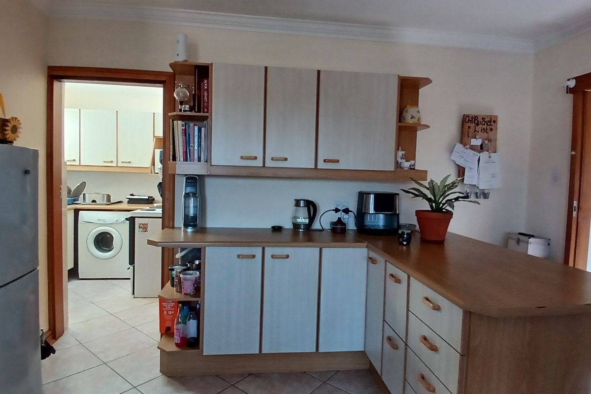 A functional kitchen featuring laminate cabinetry, ample counter space, and tiled flooring, with an adjacent laundry area visible through the doorway.