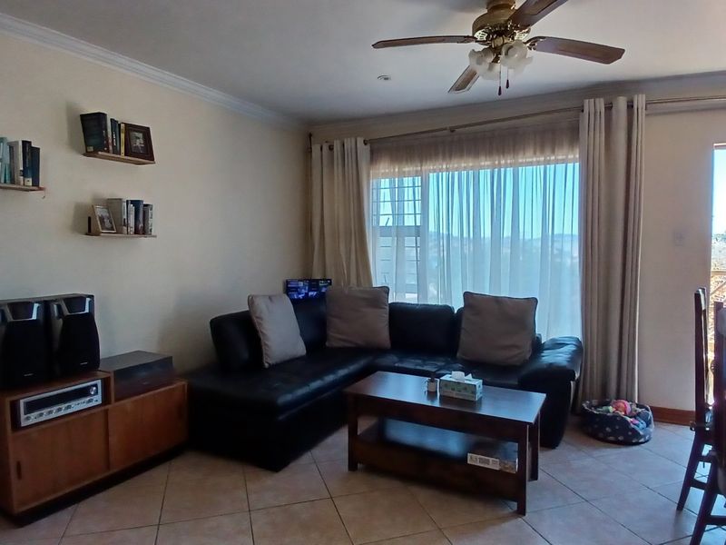 Open-plan living area featuring tiled flooring, a ceiling fan, and large sliding glass doors providing natural light and access to the balcony.