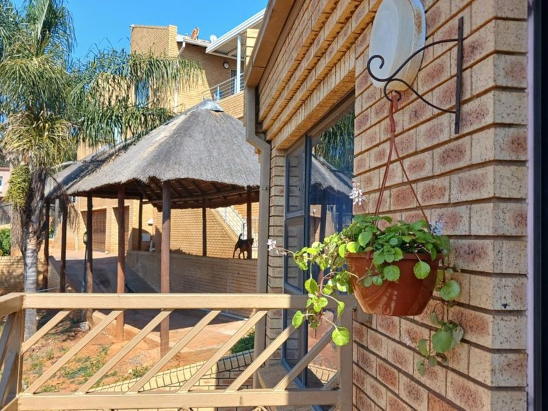 A view from a balcony featuring a brick exterior wall, metal railing, and a view of the complex grounds with a thatched gazebo.