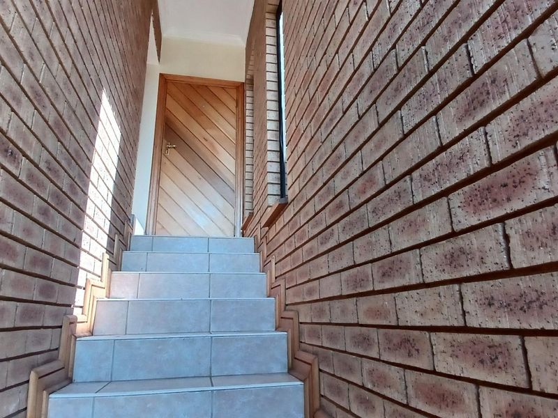An entrance area featuring a tiled staircase leading to a wooden door, framed by exposed brick walls.