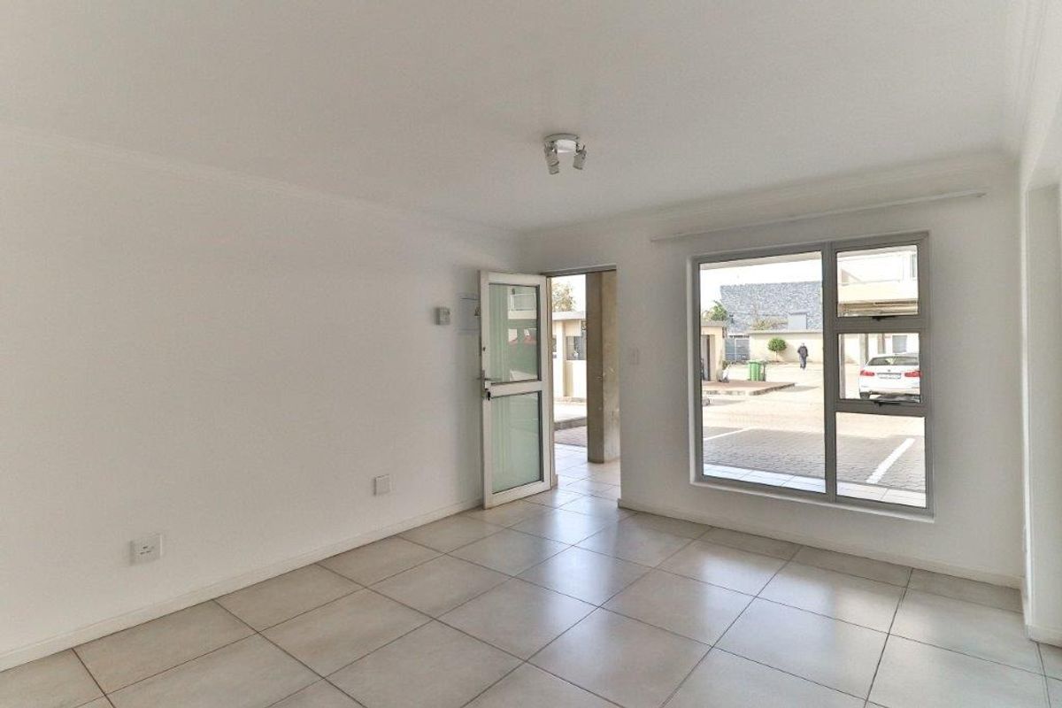 A bright, open-plan living area featuring neutral floor tiles, large windows, and direct access to the exterior.